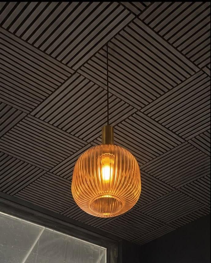 A ribbed amber pendant light glowing beneath the slatted black ceiling during renovation